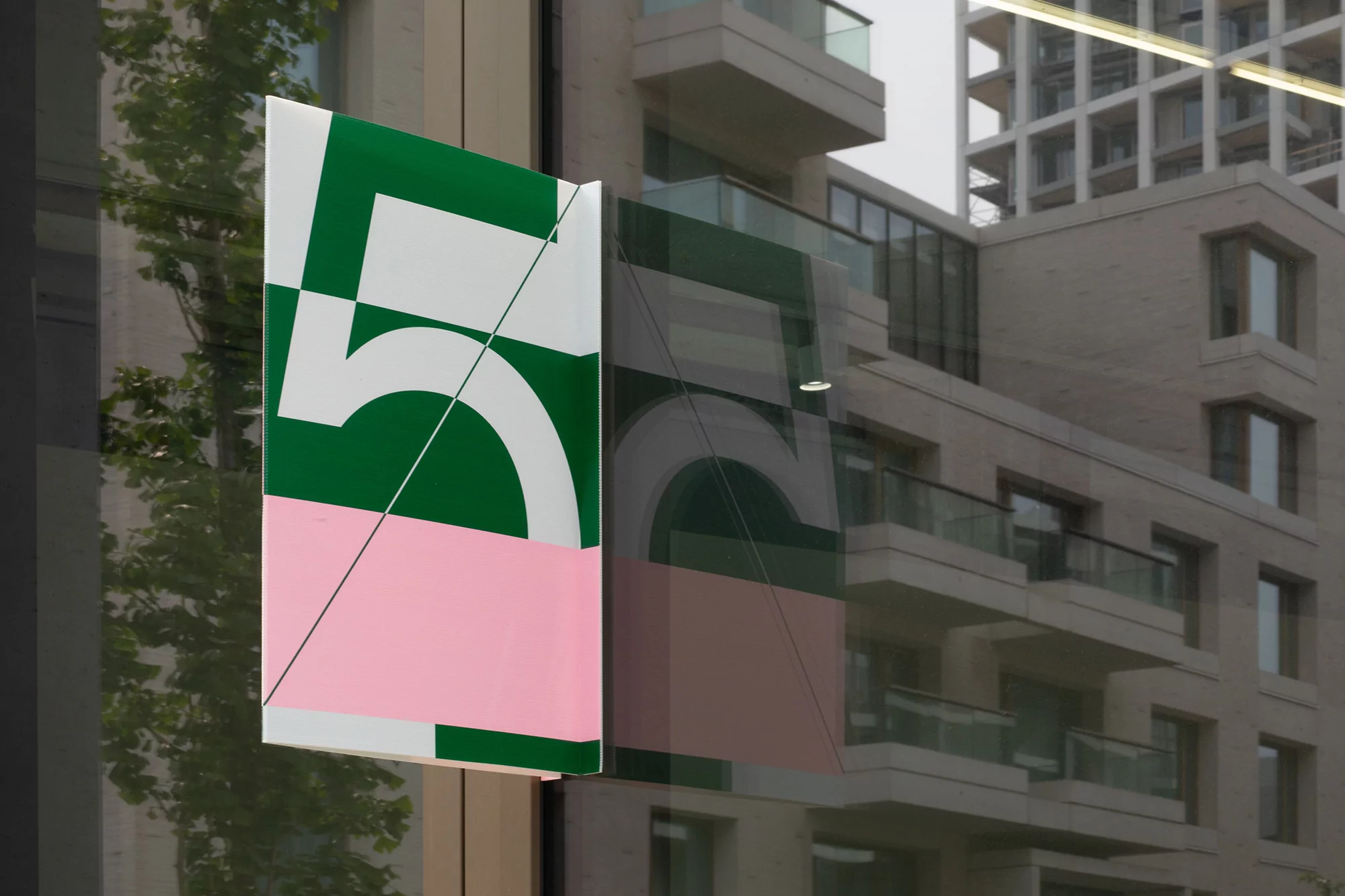 Abstract geometric shapes featuring the number five, with green, white, and pink color blocks, and reflections in a building window.