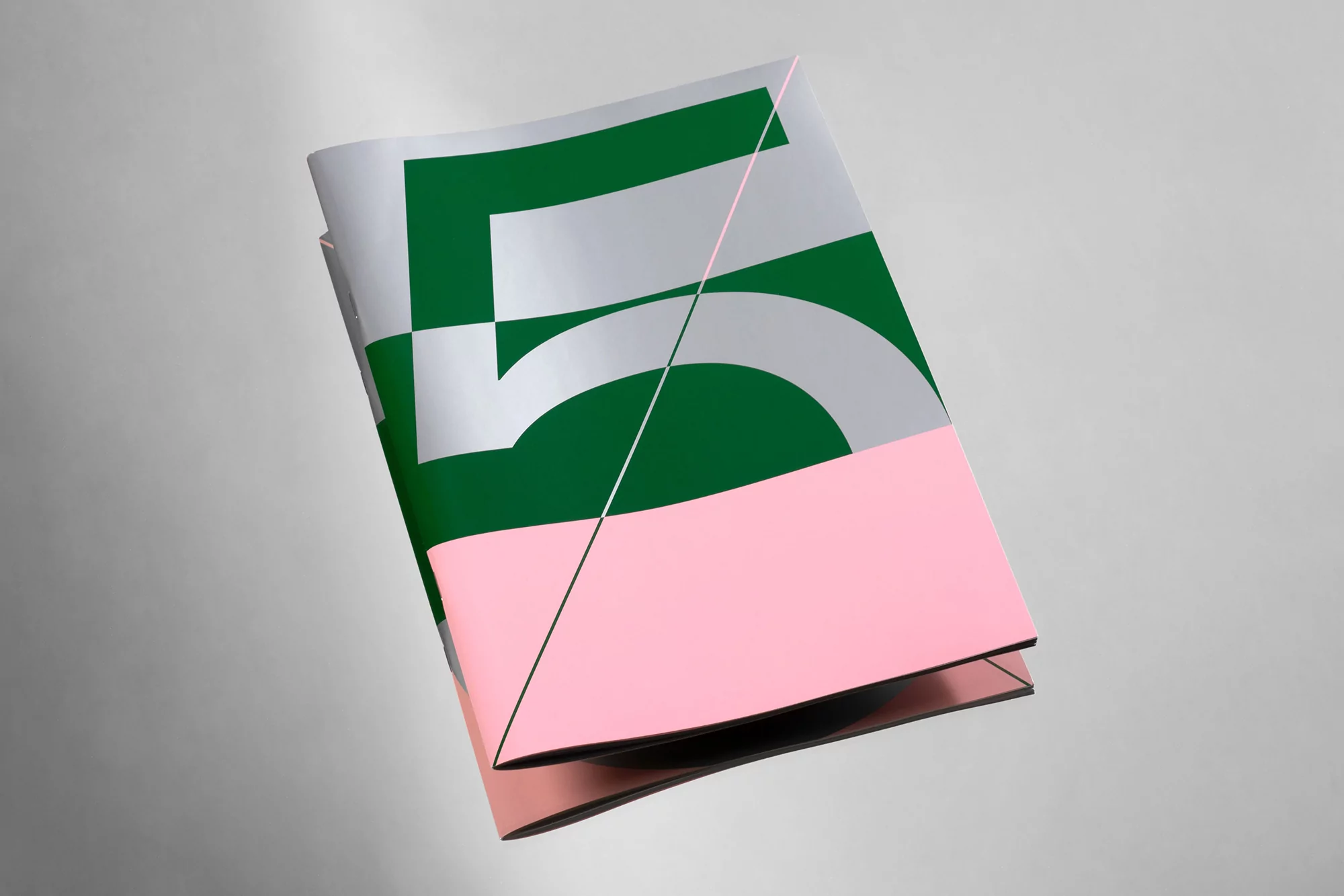 Close-up studio shot of a journal or magazine with a cover featuring green, pink, and silver geometric designs and the numeral 5.