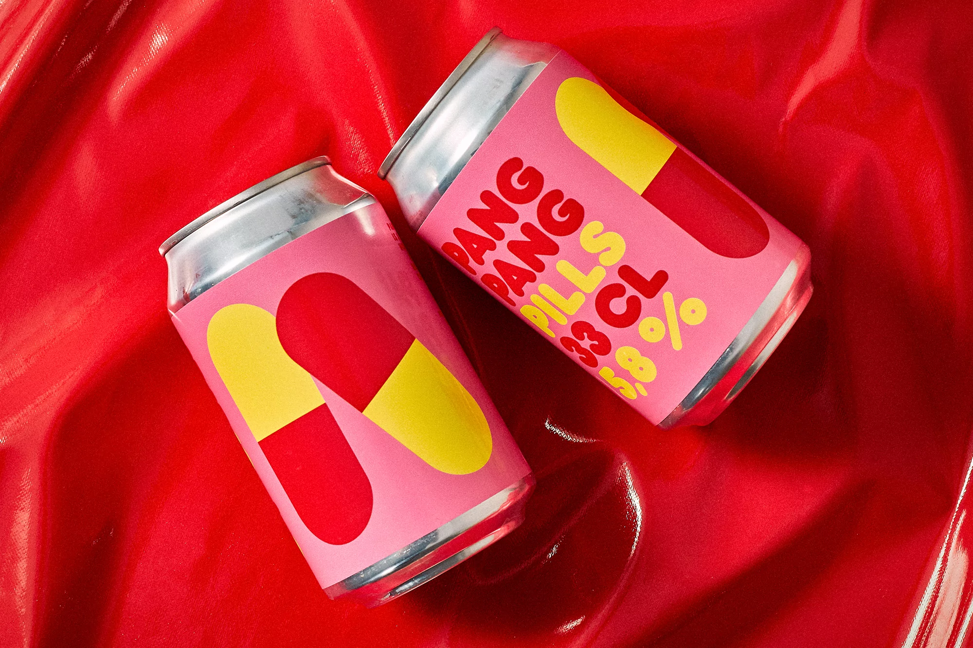 Two aluminum cans with a colorful pill design on a glossy red surface, evoking a sense of modern advertising and playful product styling.