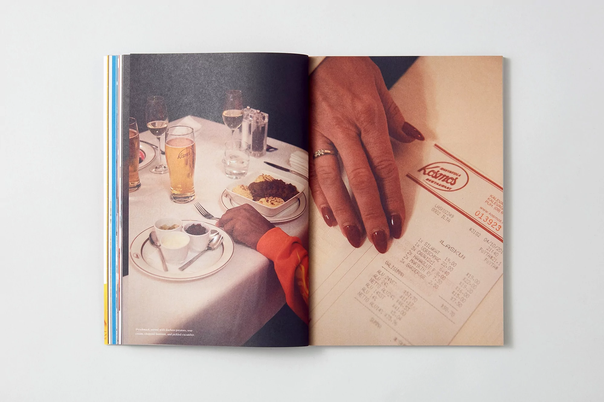 Open magazine spread featuring a table setting with food, drinks, and a restaurant bill, alongside a woman's hand with polished nails.