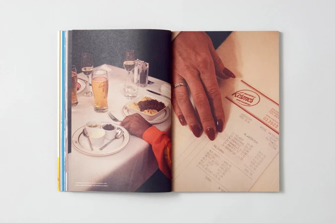 Open magazine spread featuring a table setting with food, drinks, and a restaurant bill, alongside a woman's hand with polished nails.
