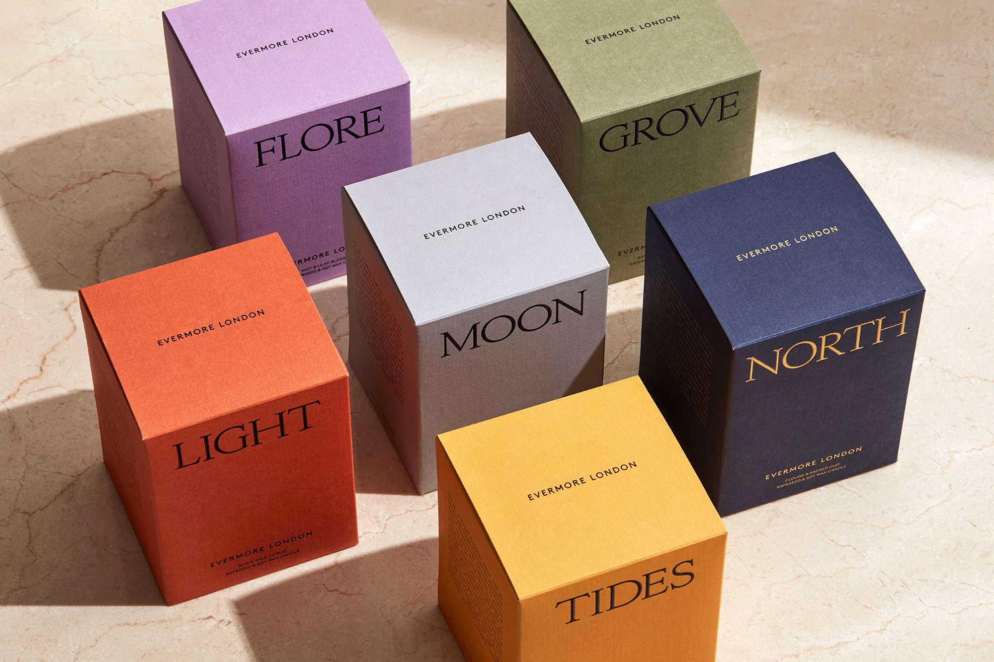Collection of Evermore London scented candles with cube-shaped packaging in various colors on a marble surface, product photography.
