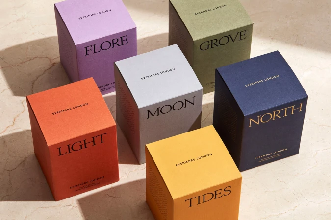 Collection of Evermore London scented candles with cube-shaped packaging in various colors on a marble surface, product photography.