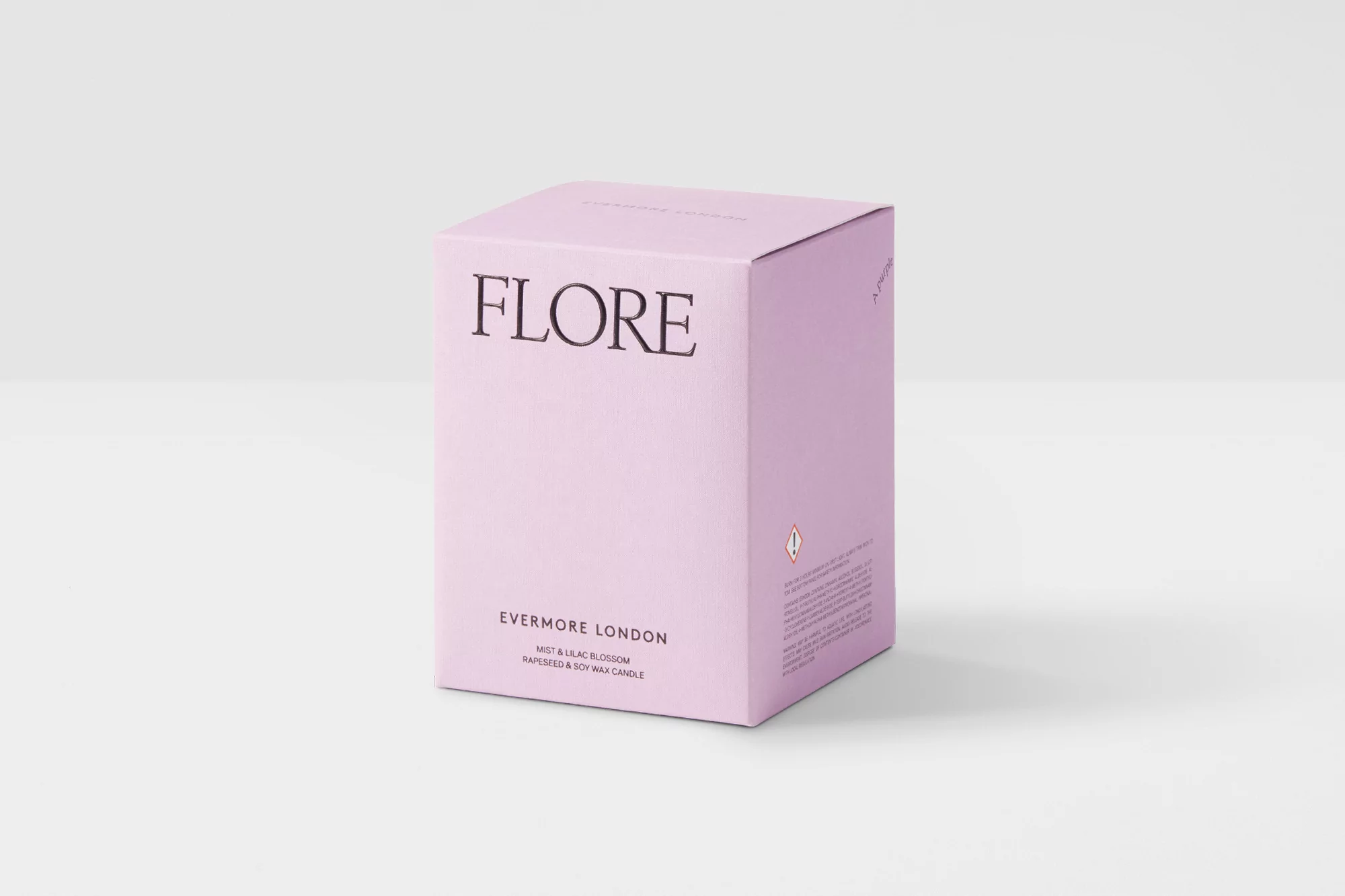 Studio shot of a light-purple square box of 'FLORE Evermore London' mist and lilac blossom rapeseed and soy wax candle on a white background.