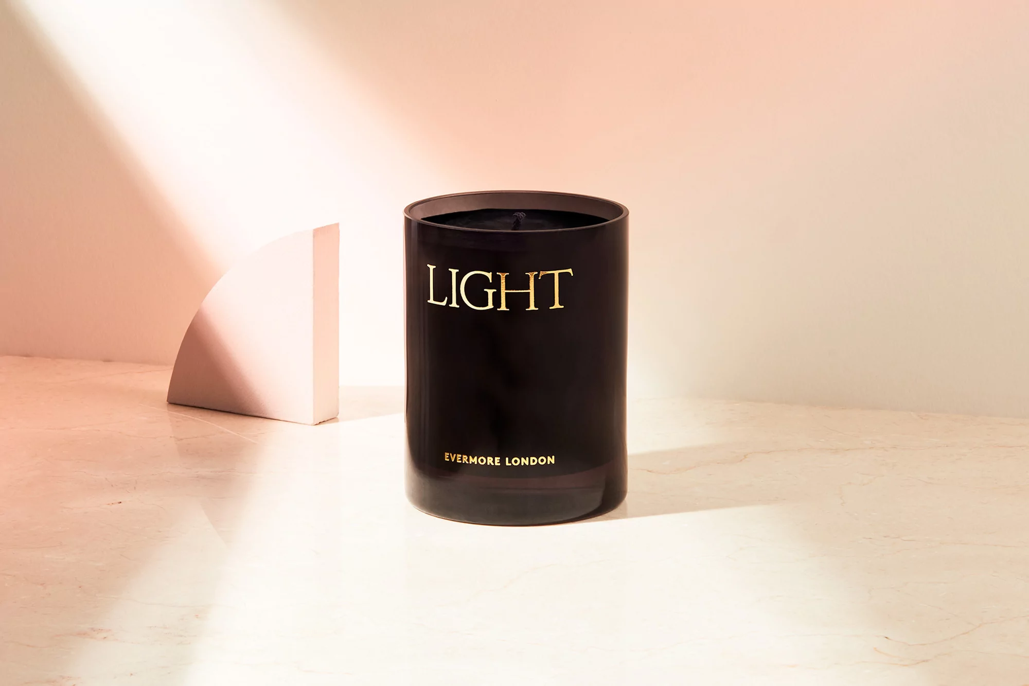 Close-up of a black Evermore London candle on a marble surface with light patterns and a geometric object in the background.