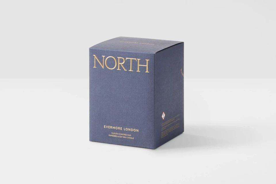 Close-up of a blue Evermore London candle box with gold lettering spelling 'NORTH' on a white background. Minimalist aesthetic.