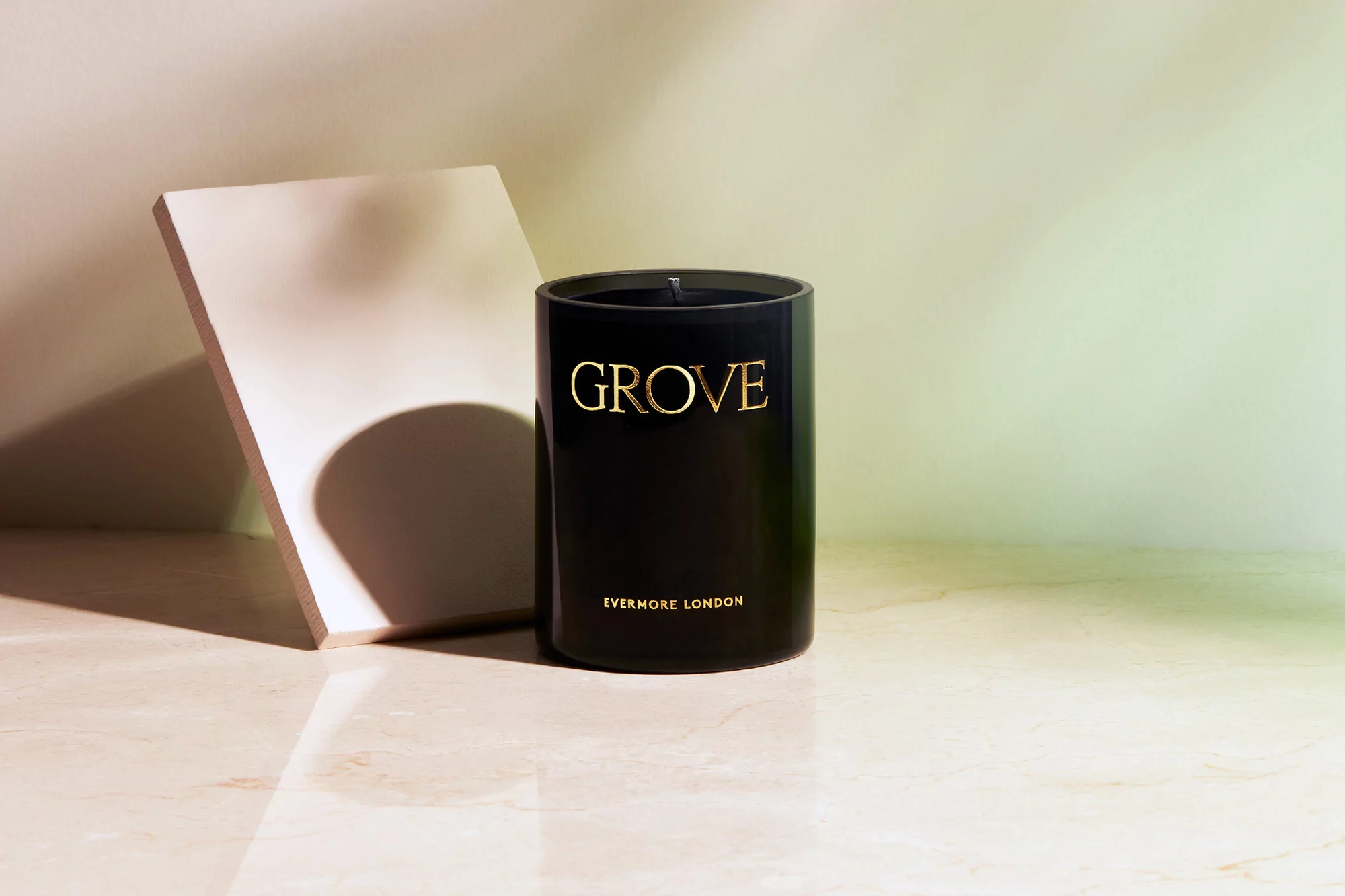 Studio product shot of a black Evermore London candle with gold lettering, set on a reflective marble surface with a neutral backdrop.