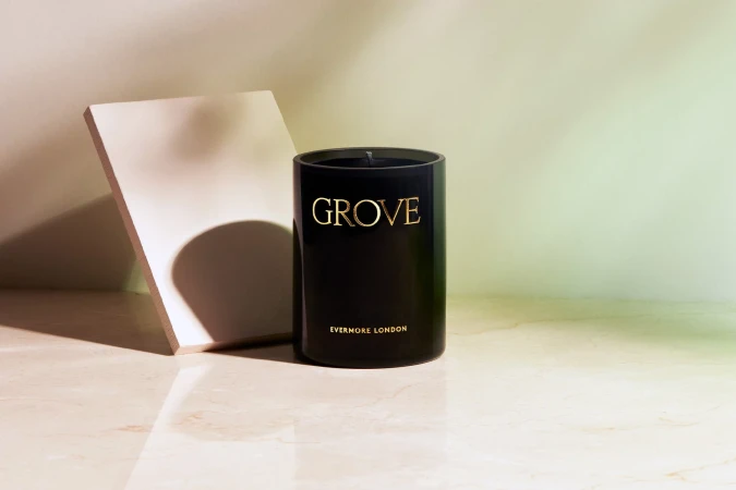 Studio product shot of a black Evermore London candle with gold lettering, set on a reflective marble surface with a neutral backdrop.