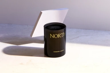 Black cylindrical candle jar with gold text reading NORTH and EVERMORE LONDON on a light marble surface.
