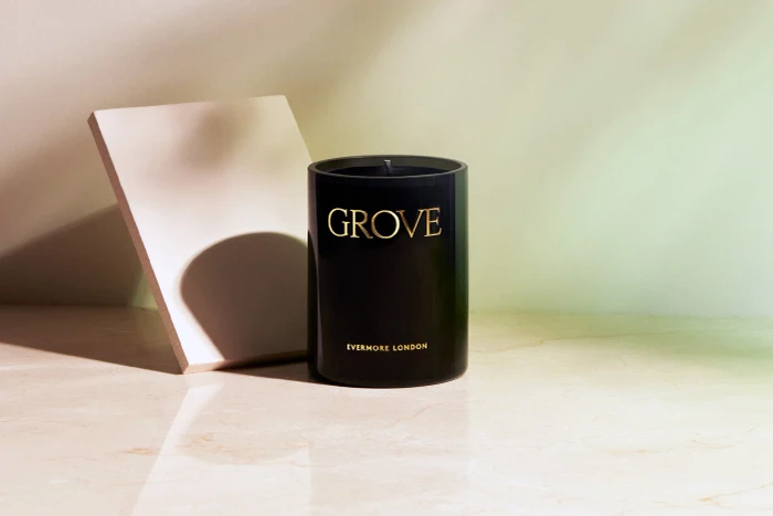 Black candle jar with gold text reading GROVE and Evermore London on a marble surface next to a geometric block