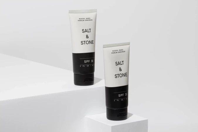 Two white tubes of Salt & Stone SPF 30 sunscreen sit on white geometric platforms against a white backdrop in a studio setting.
