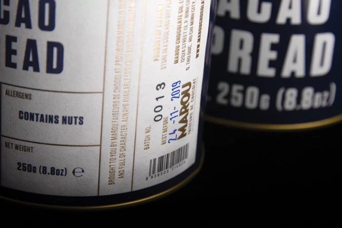 Two cans of Marou cacao spread featuring allergen and nutritional information against a dark background in a studio shot.