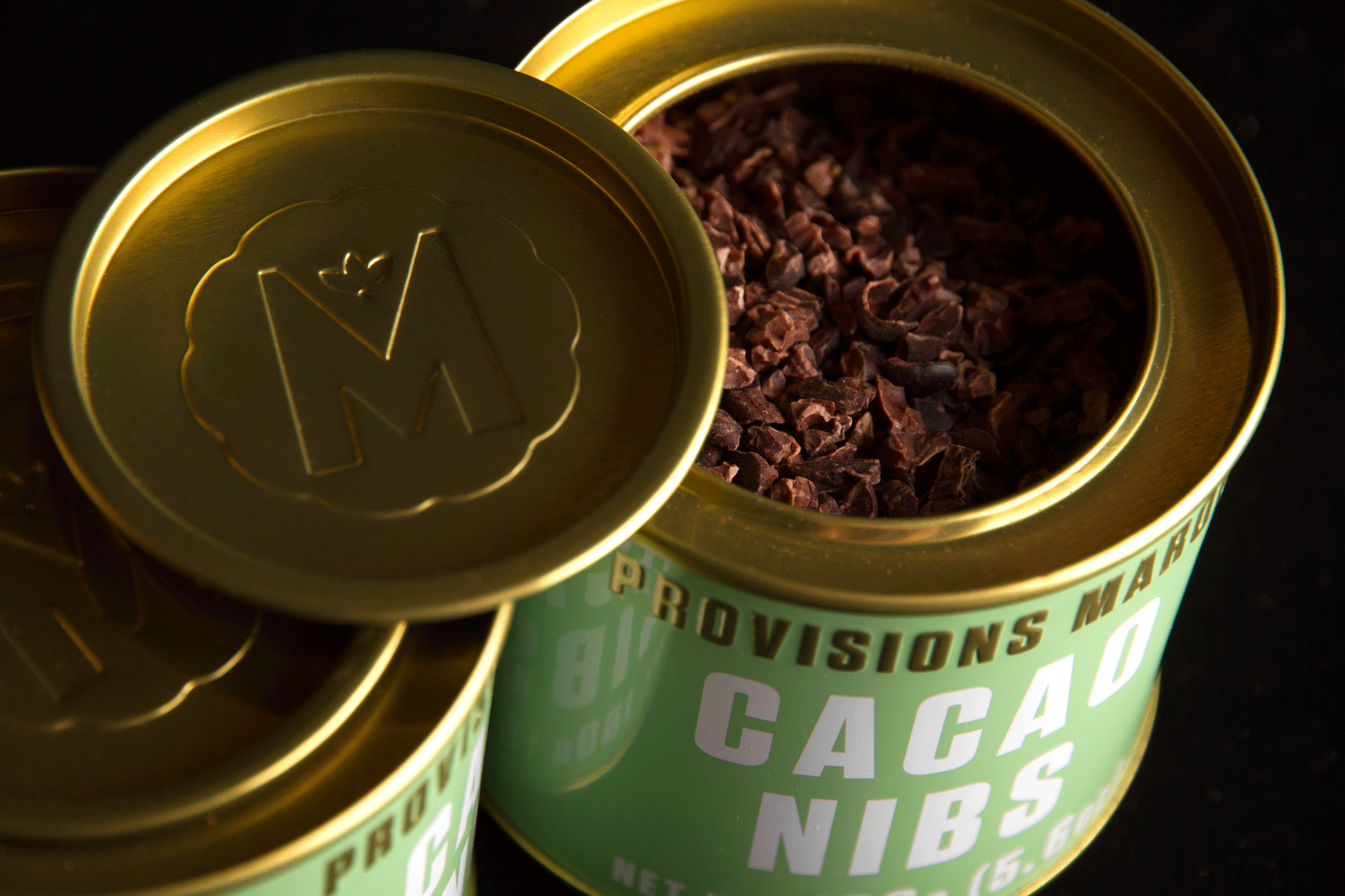 Close-up studio shot of Marou Provisions cacao nibs in a gold tin can with the lid resting on the side, offering a detailed view.
