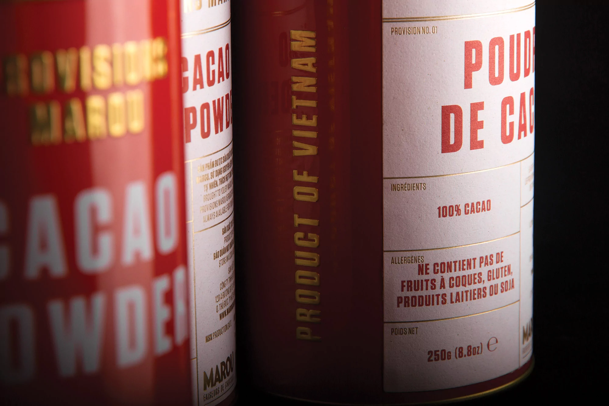 Close-up of Marou cacao powder cans, featuring red and white packaging with gold lettering, highlighting 'Product of Vietnam'.