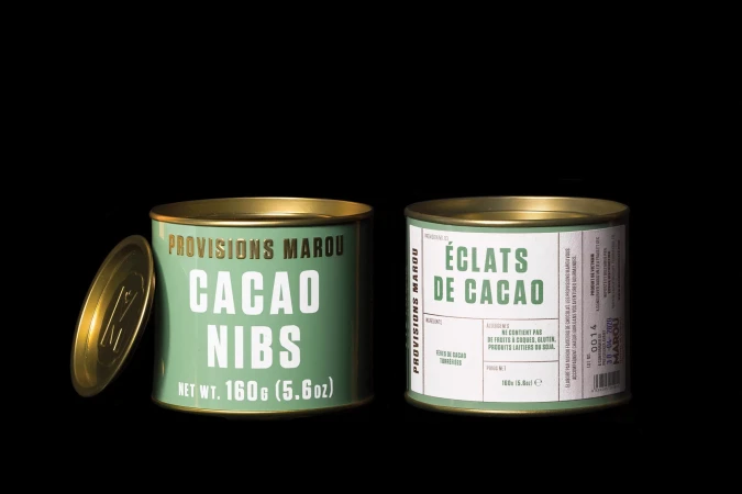 Two green tins of Provisions Marou cacao nibs and éclats de cacao are displayed against a black backdrop in a product shot.