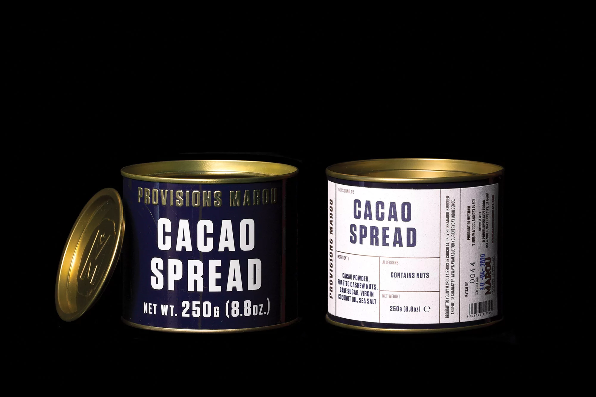 Two cans of Marou Cacao Spread are presented on a black surface; one can is open, revealing its golden lid, next to a sealed can.