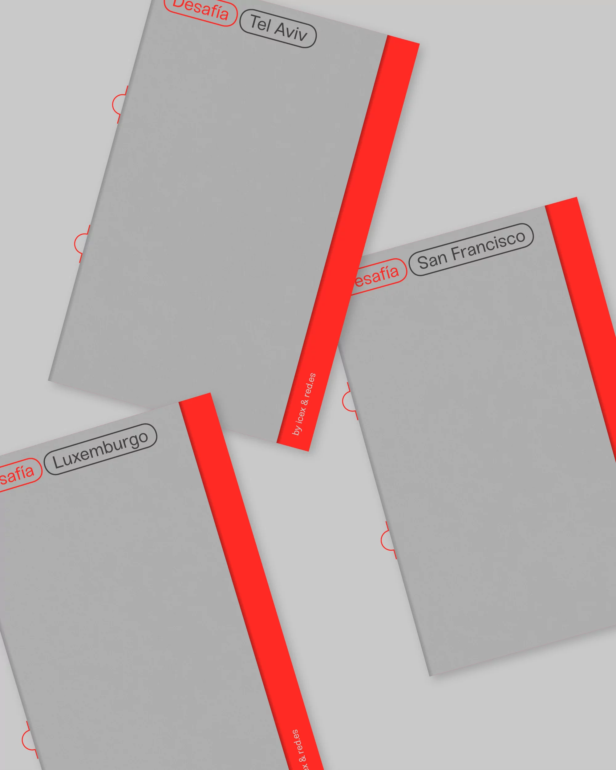 Three closed books with red spines titled 'Desafia Tel Aviv', 'Desafia San Francisco', and 'Desafia Luxemburgo' on a neutral gray background.