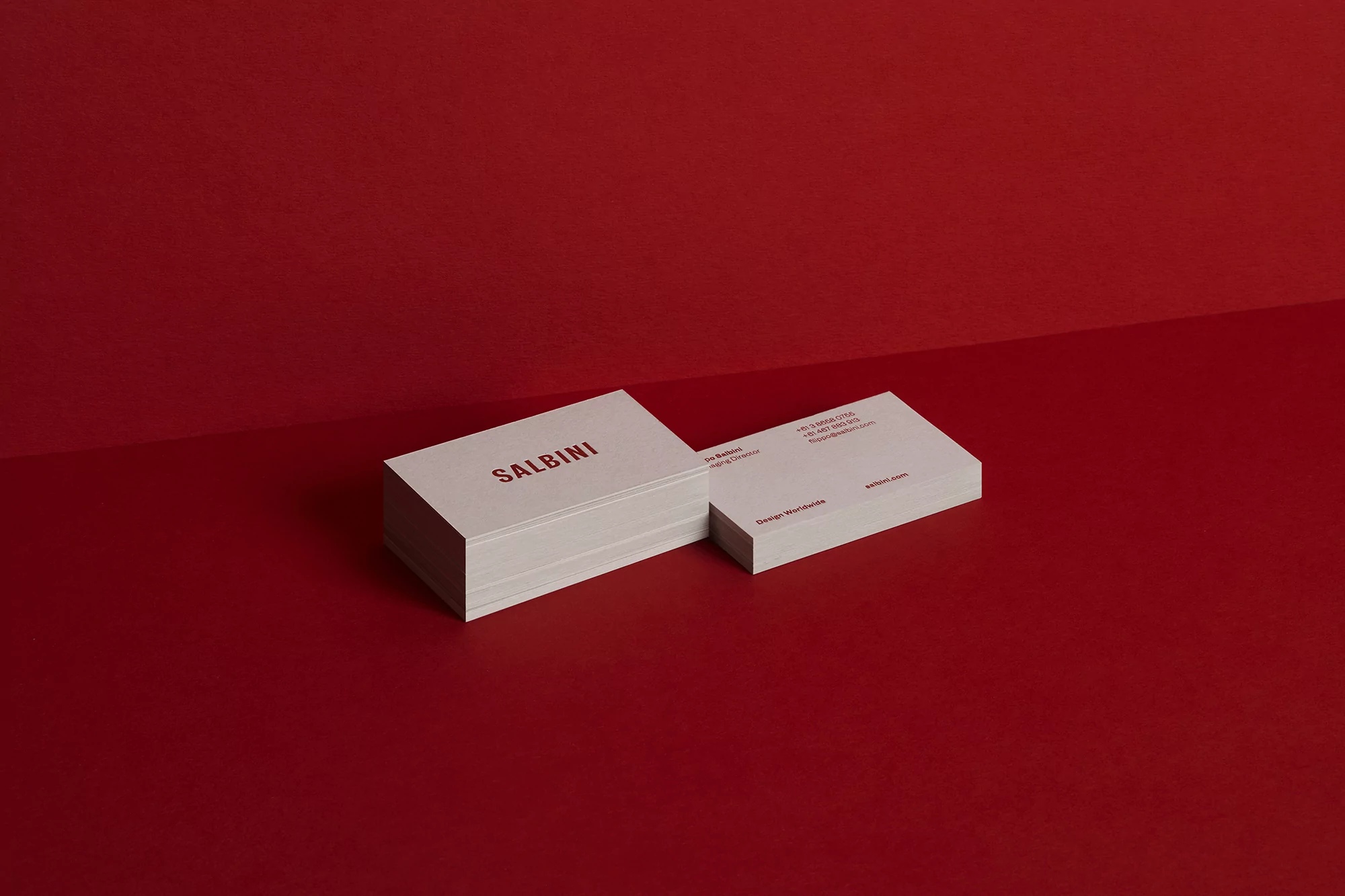 Stack of clean white business cards with red text branding against a red background. Minimalist business card design and presentation.