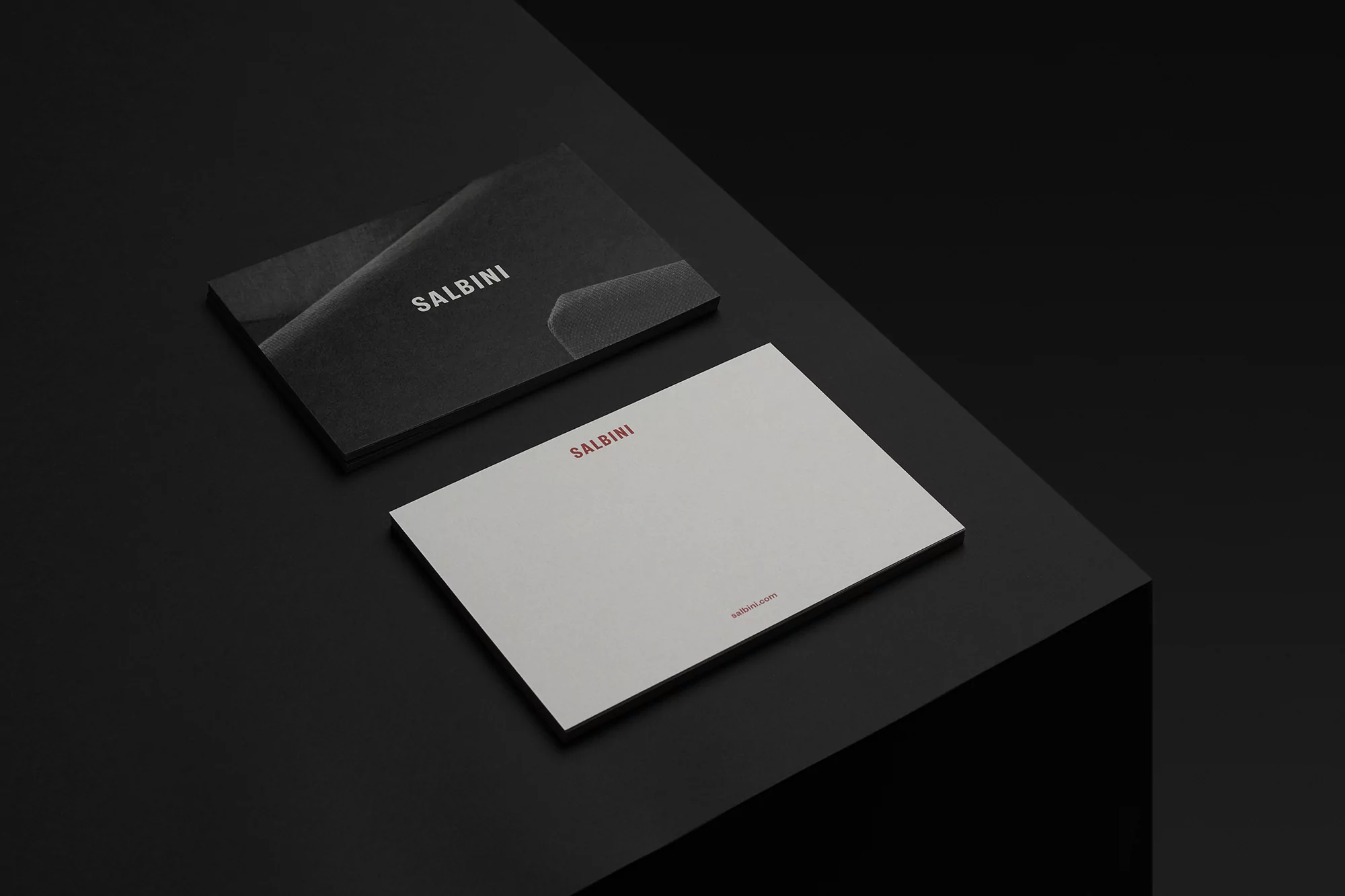 Two Salbini cards on a black surface, one in black and one in white, in a minimalist studio product shot promoting design.