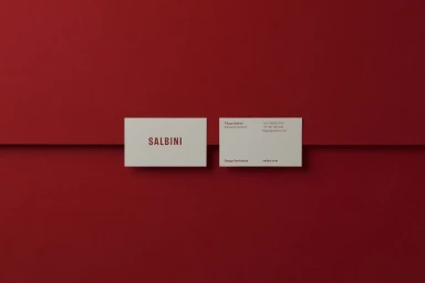 Two white business cards resting against a deep red background with minimalist typographic branding.