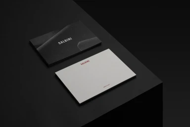 Salbini brand stationery featuring a black business card and white letterhead on a dark surface