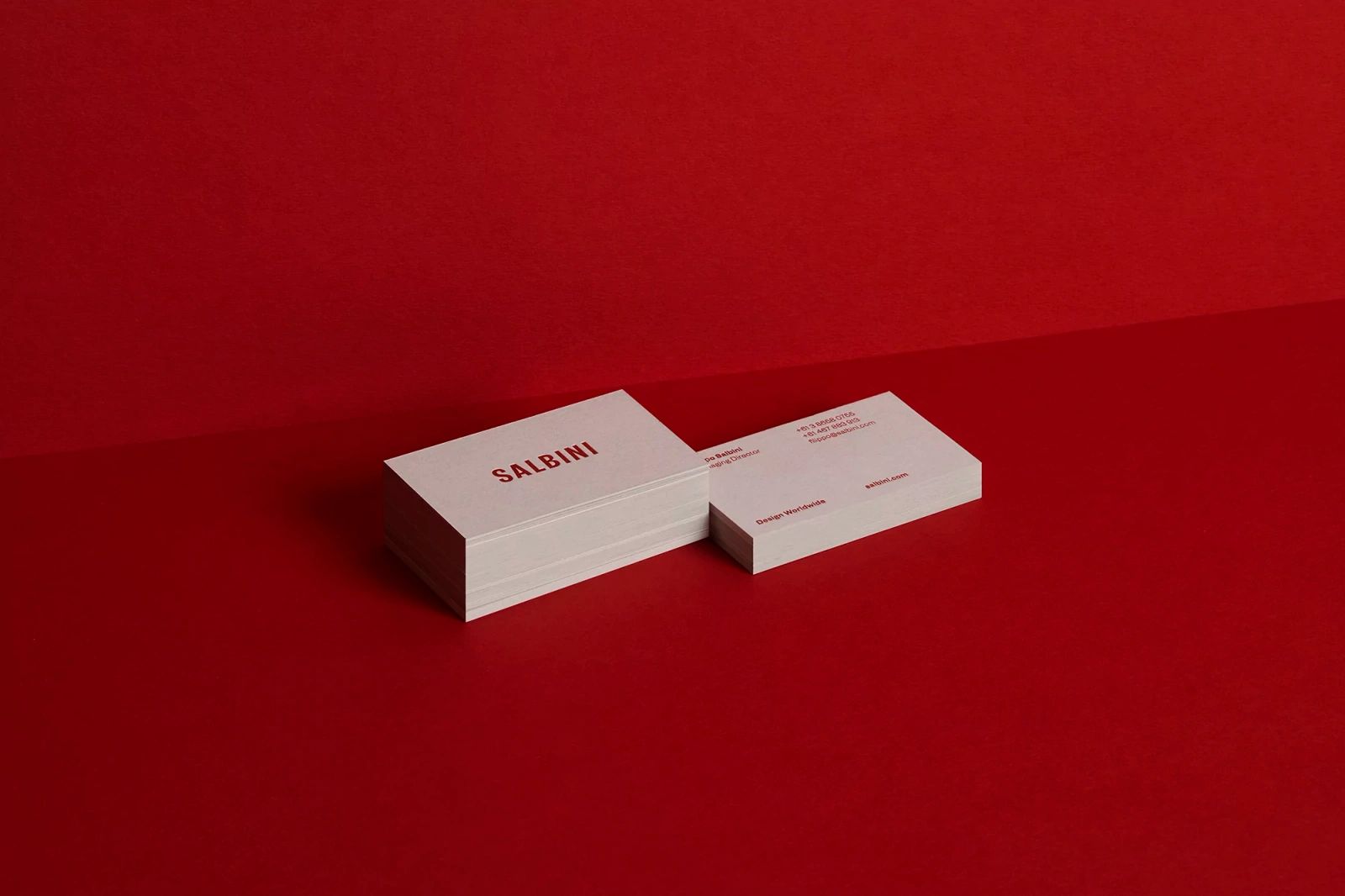 Stacks of white business cards with red Salbini branding on a rich red textured surface
