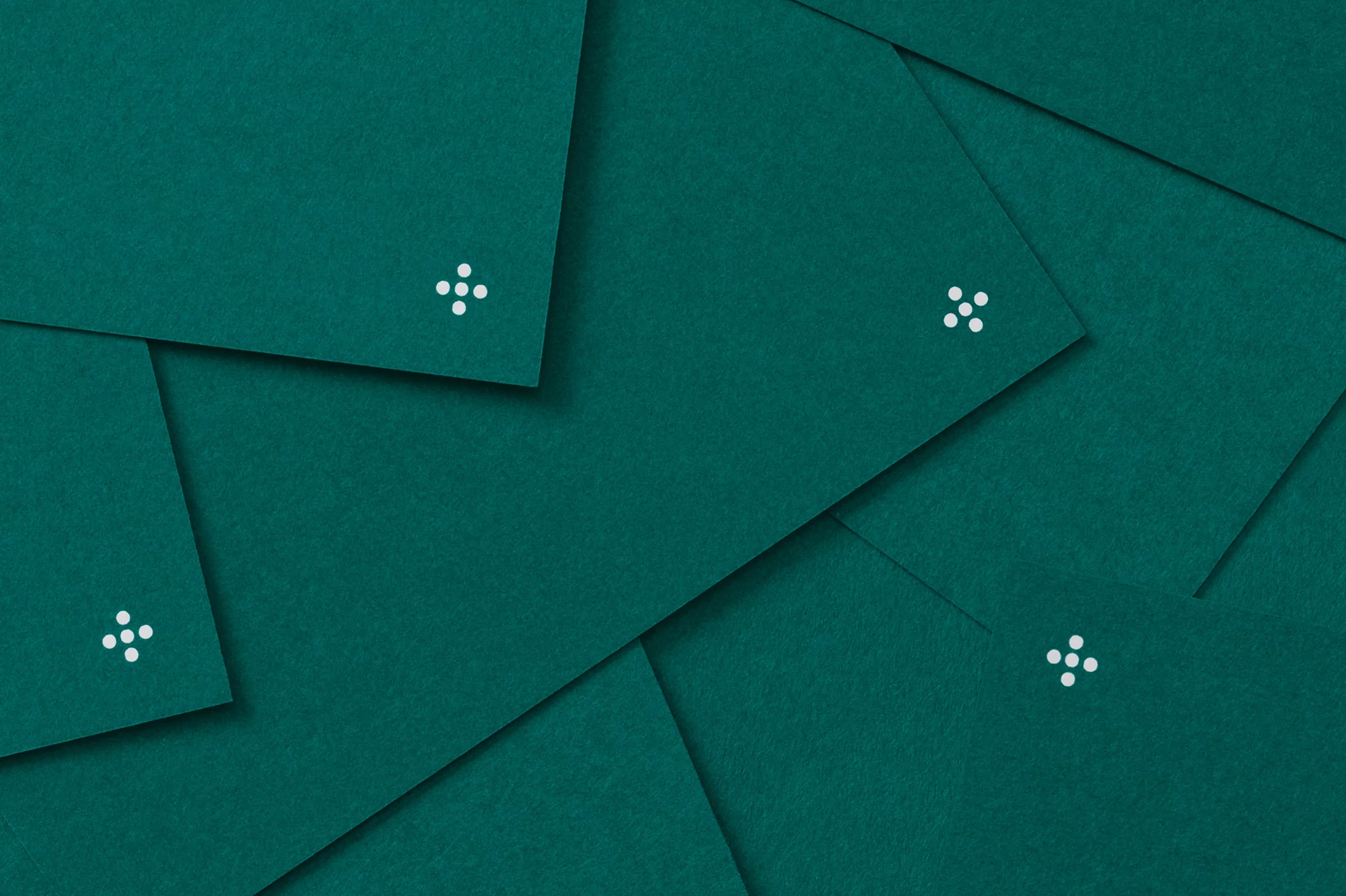 Overlapping textured dark teal green paper with a small white graphic on each sheet, creating a layered geometric pattern.