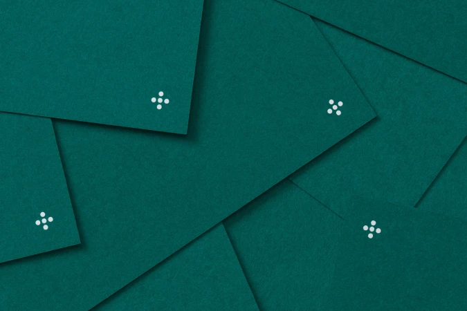 Overlapping textured dark teal green paper with a small white graphic on each sheet, creating a layered geometric pattern.