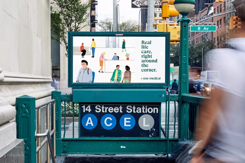 An outdoor advertisement for One Medical featuring illustrated diverse people, set above a 14 Street Station subway entrance in New York City.