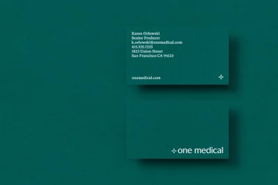 Two green business cards for One Medical featuring white serif typography and logo against a dark teal textured paper background.
