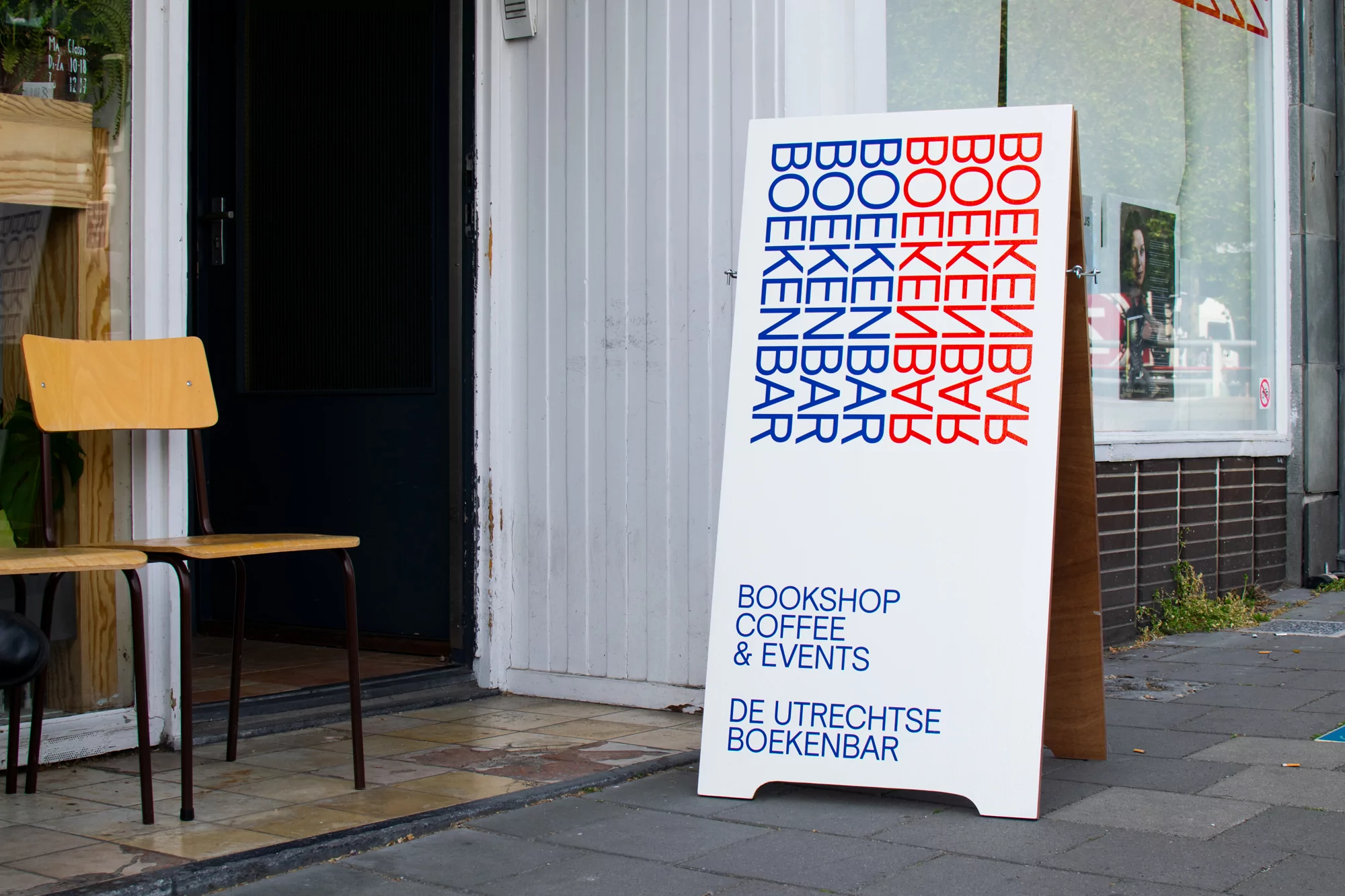 Bookshop sidewalk sign with painted lettering and chair outside a storefront, advertising coffee and events in an urban setting.