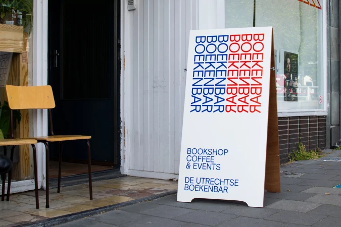 Bookshop sidewalk sign with painted lettering and chair outside a storefront, advertising coffee and events in an urban setting.