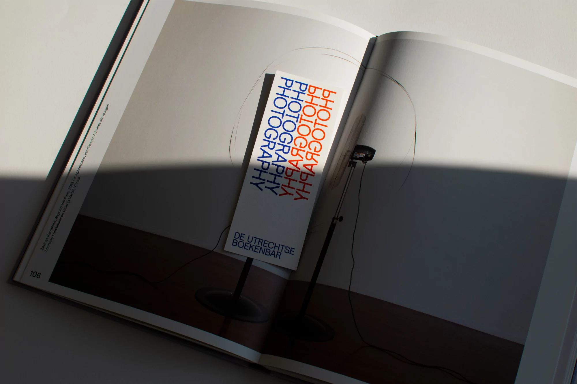 Book lies open featuring a floor lamp photo with a red, white, and blue bookmark, casting a shadow on the left page.