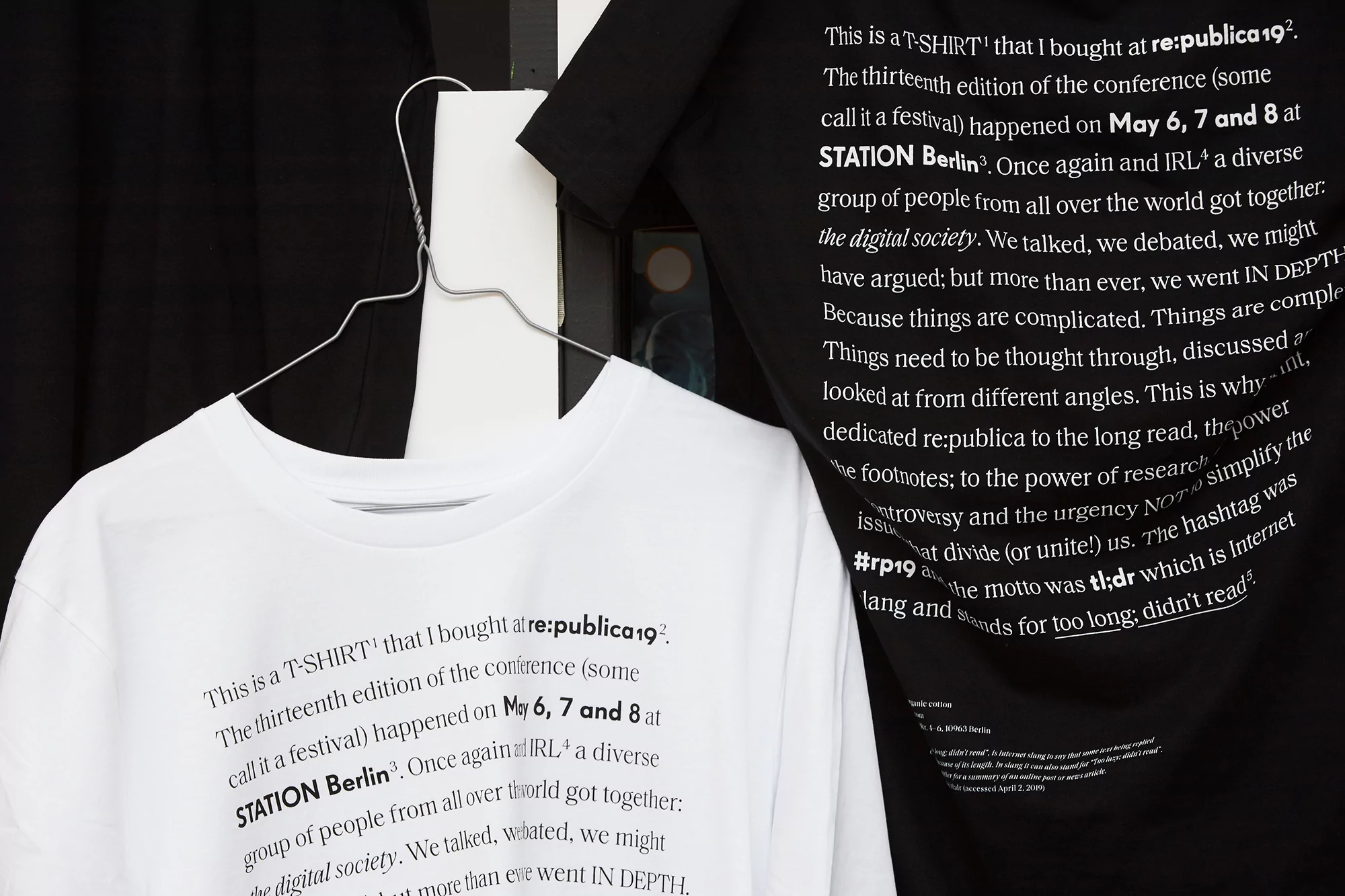 Two t-shirts, one white and one black, hanging on a rack. Each has text about the re:publica 19 conference printed on the front.