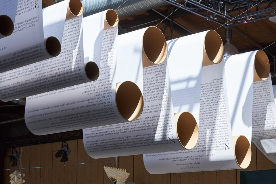 Close-up of an art installation featuring rolled paper tubes suspended from the ceiling, filled with text, creating an immersive textual environment.