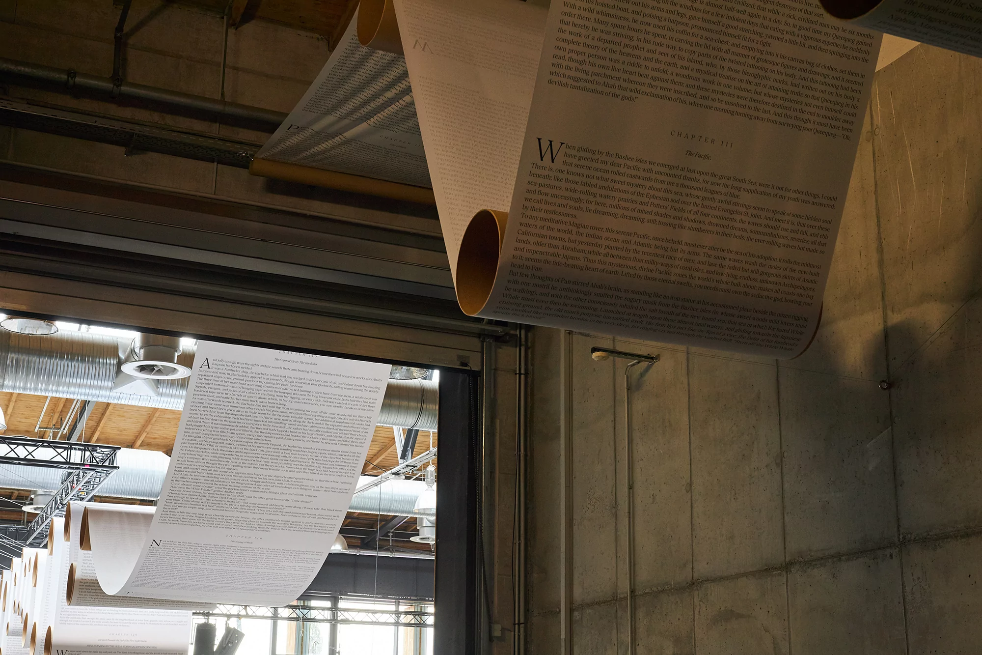 Indoor view of a unique art installation featuring scrolls of printed text hanging from the ceiling, creating an immersive literary environment.