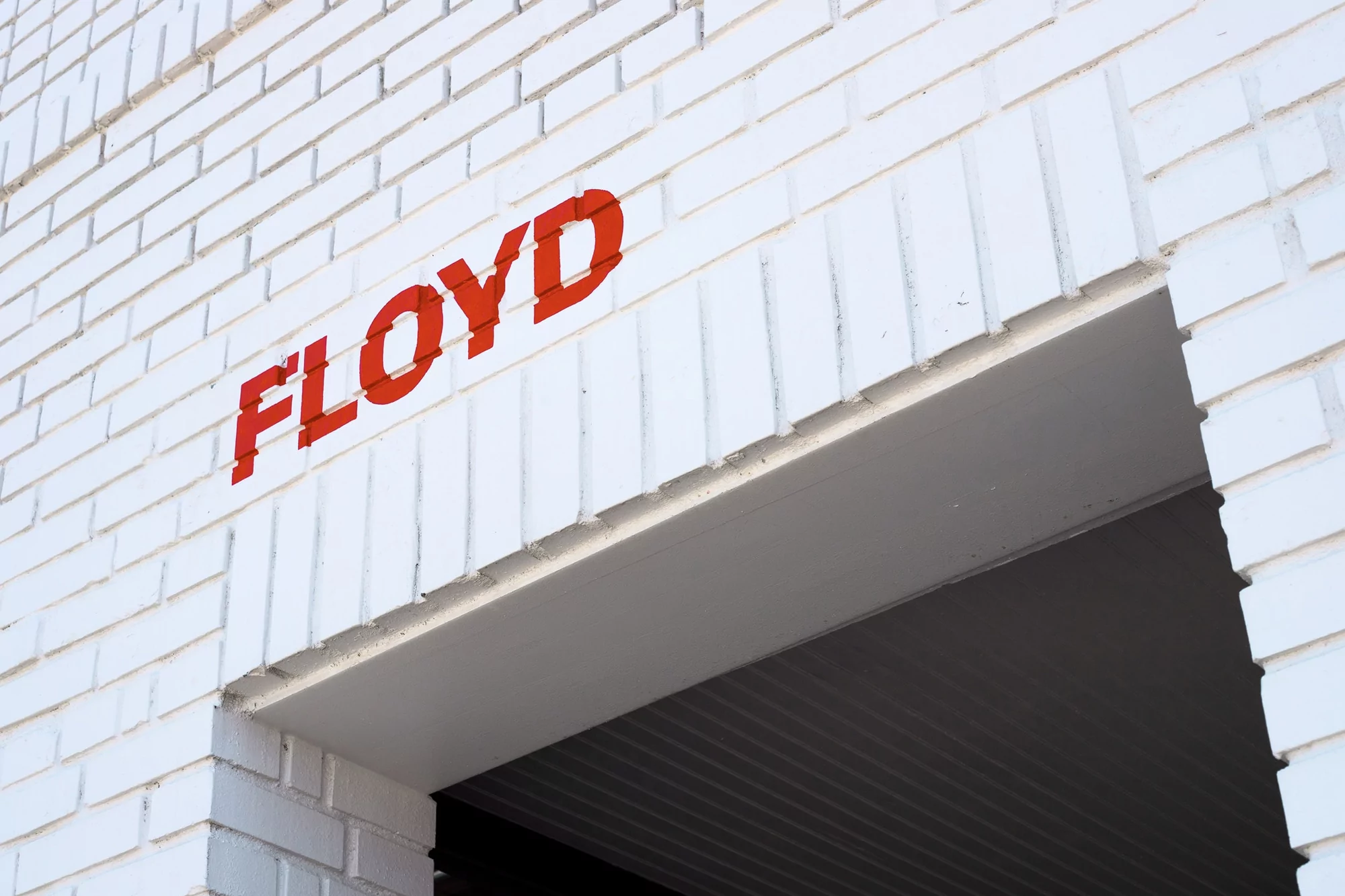 Exterior of a white brick building featuring the word 'FLOYD' in red lettering above the entrance or doorway.