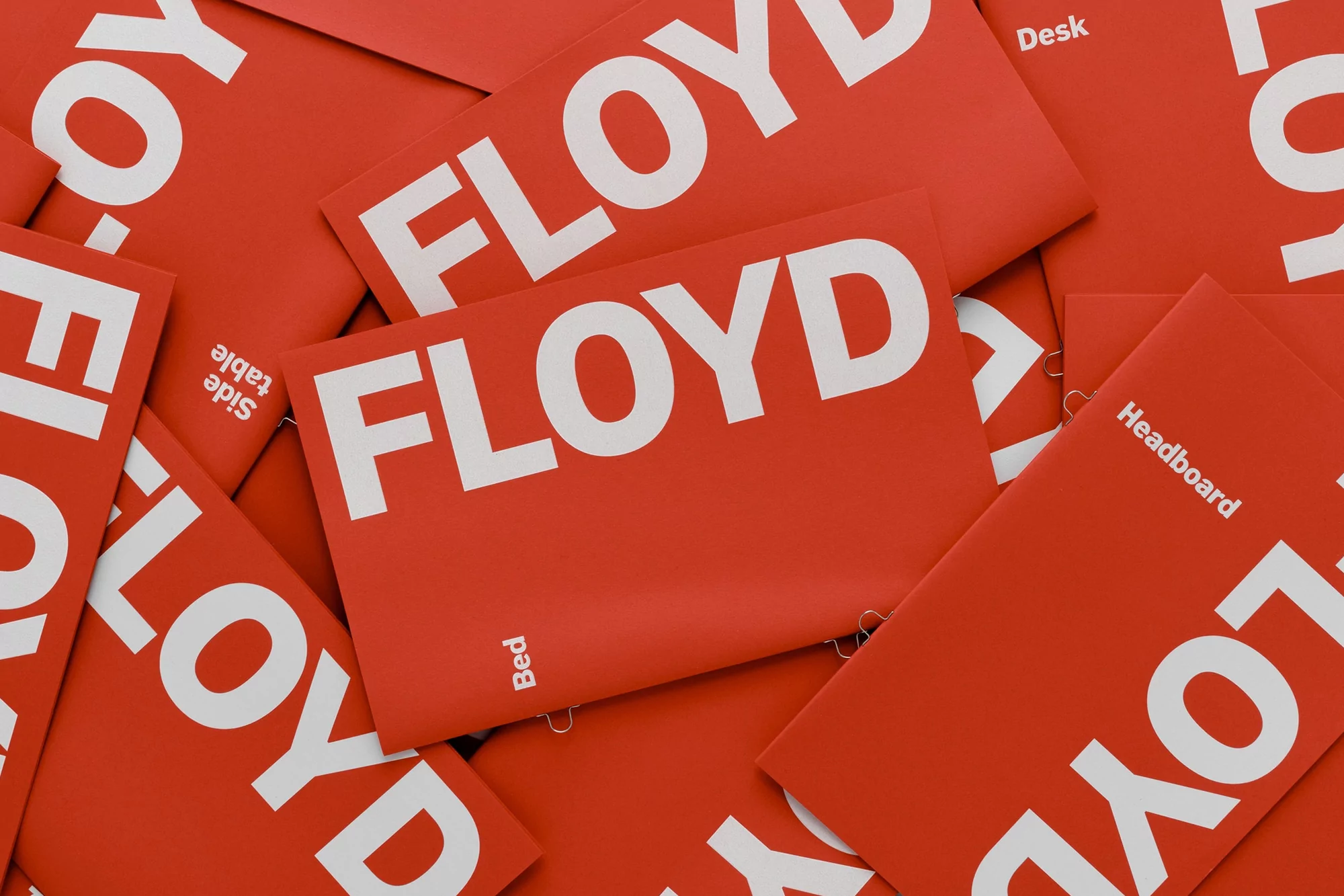 Stack of vibrant red cards featuring the brand name FLOYD in bold white letters and promoting furniture, including beds, desks, and headboards.