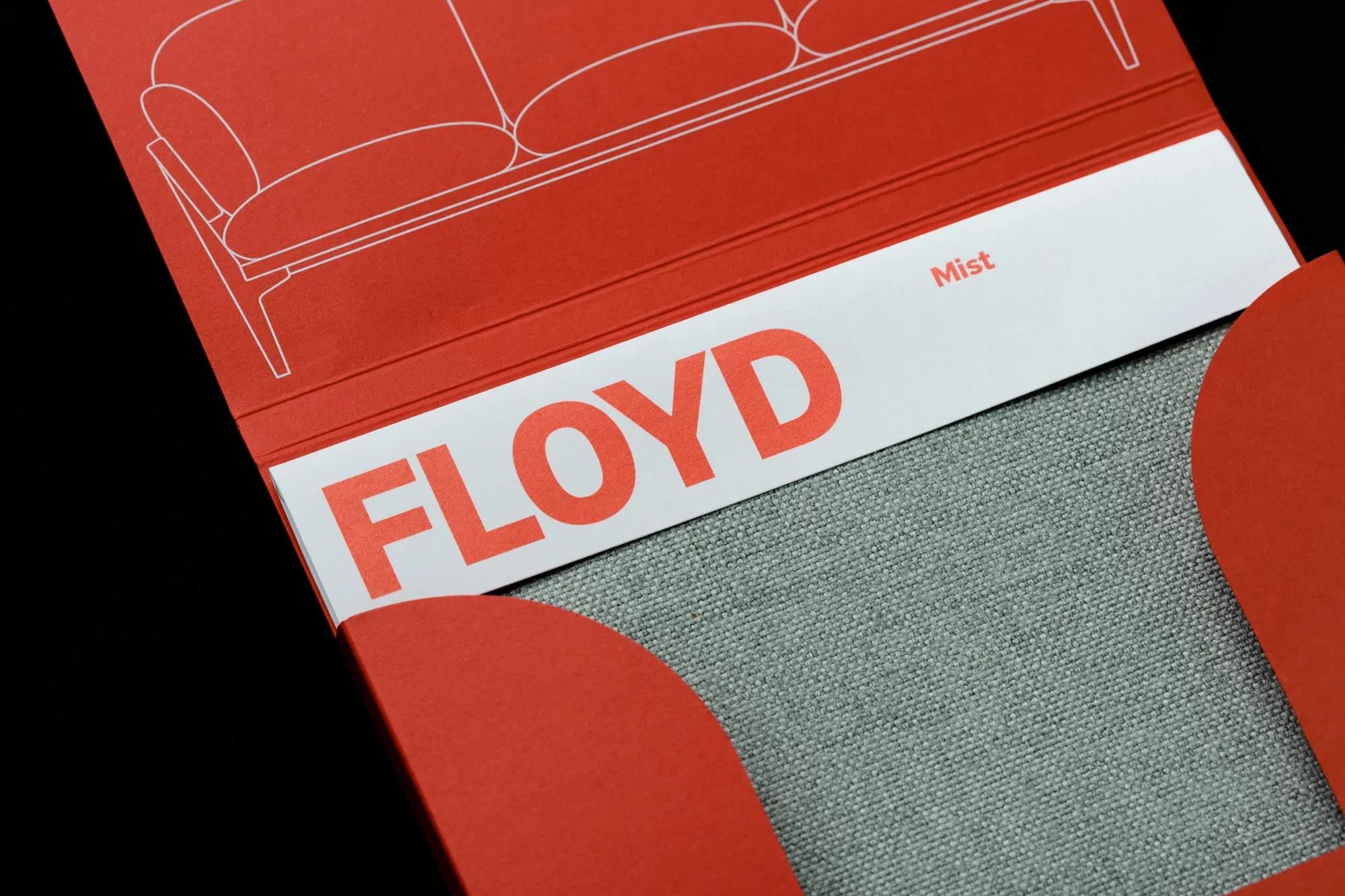 Product shot of a Floyd brand sofa sample in a coral paper holder with a gray fabric sample for interior design and color palette.