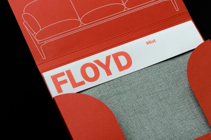Product shot of a Floyd brand sofa sample in a coral paper holder with a gray fabric sample for interior design and color palette.