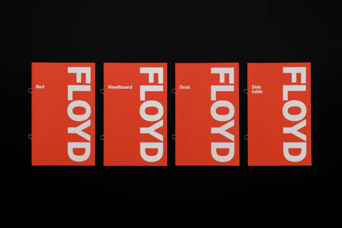 Four coral-colored panels displaying 'FLOYD' vertically in white. Panels advertise furniture: bed, headboard, desk, and side table.