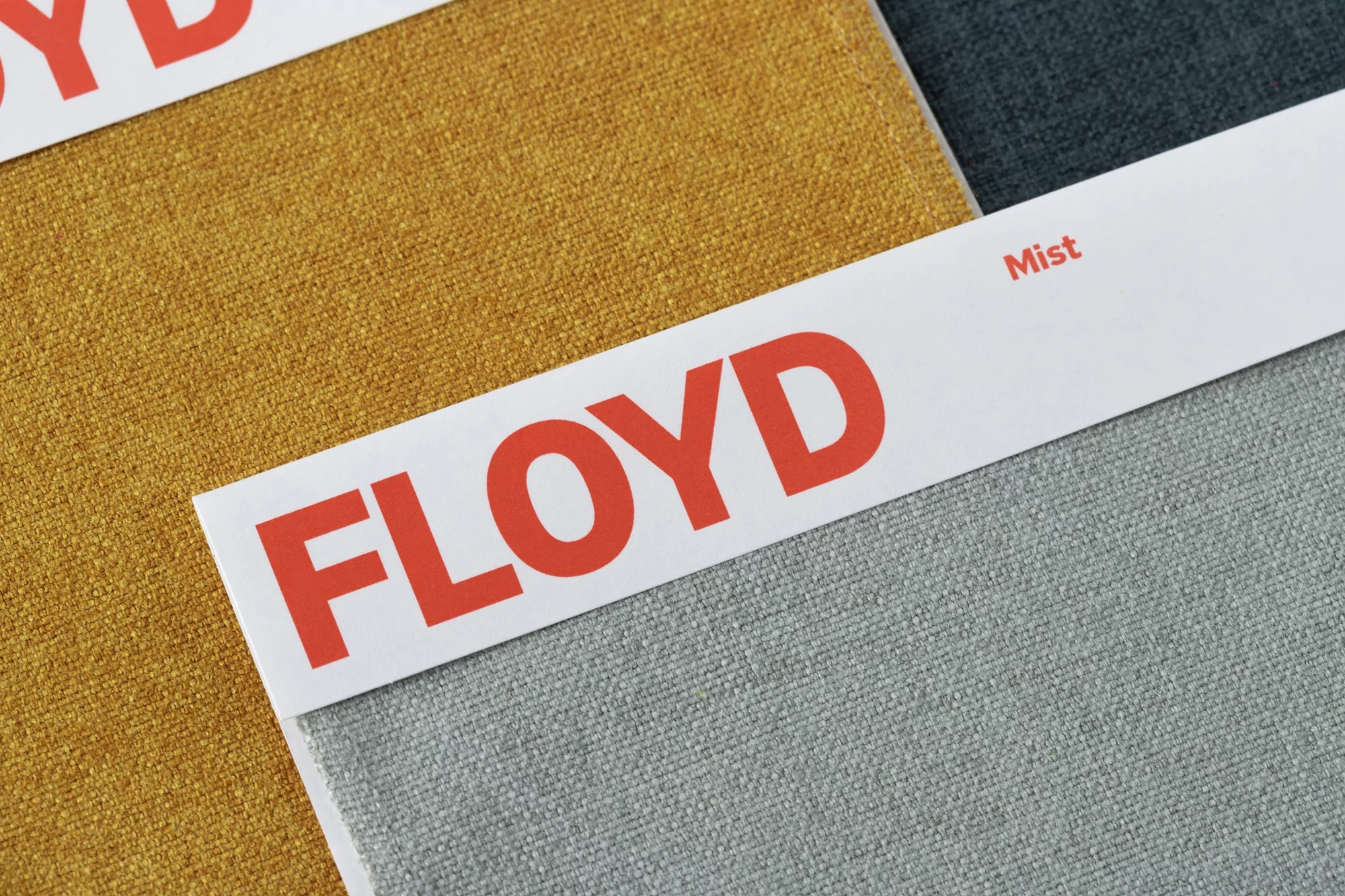 Close-up of 'Floyd' branded fabric swatches in mustard and grey, showcasing texture and color variations for design and upholstery.