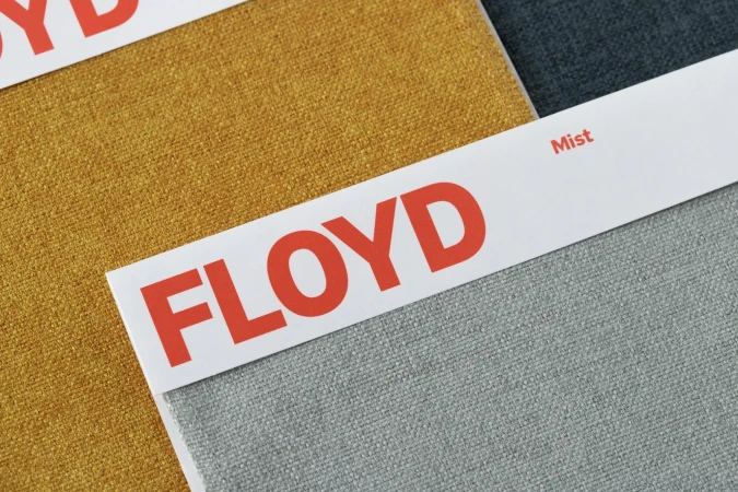 Close-up of 'Floyd' branded fabric swatches in mustard and grey, showcasing texture and color variations for design and upholstery.