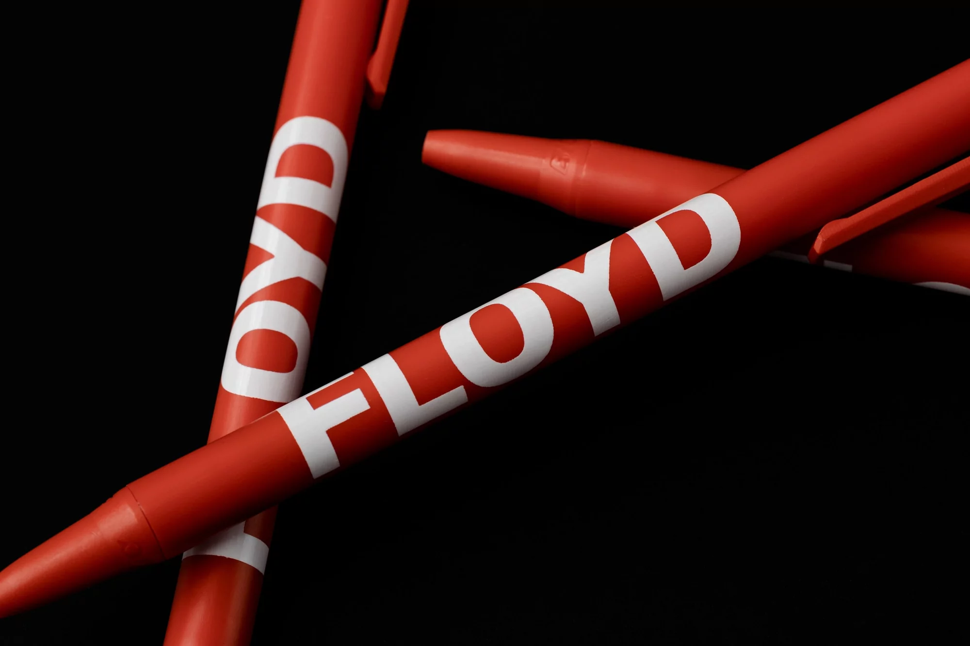 Close-up studio shot of several red ballpoint pens with white 'Floyd' text against a black background, showcasing a clean product image.