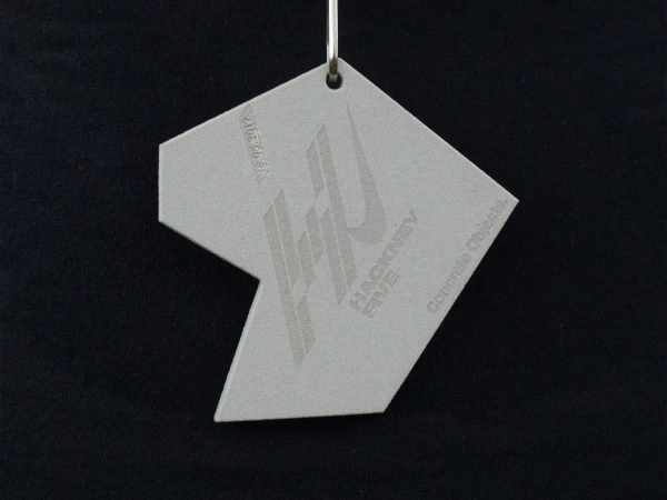 Close-up of a geometric gray tag with a design and text, hanging from a metal ring against a black background. Minimalist design.