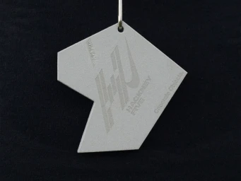 Grey polygonal pendant featuring debossed typographic branding against a solid black background