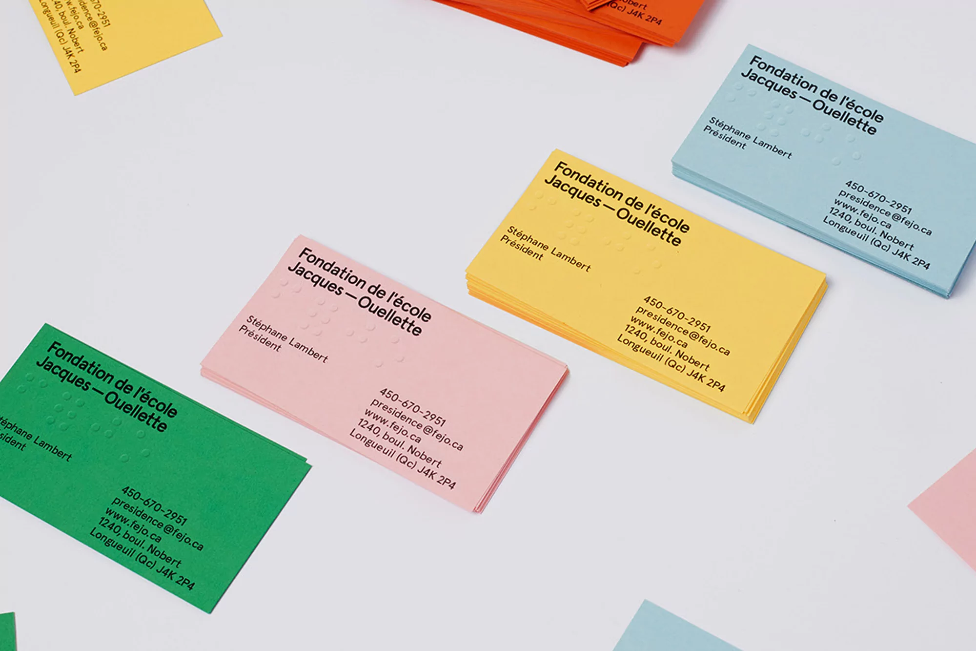 Stacks of colorful business cards with braille sit on a white surface, displayed in a clean, minimalist, and modern aesthetic.