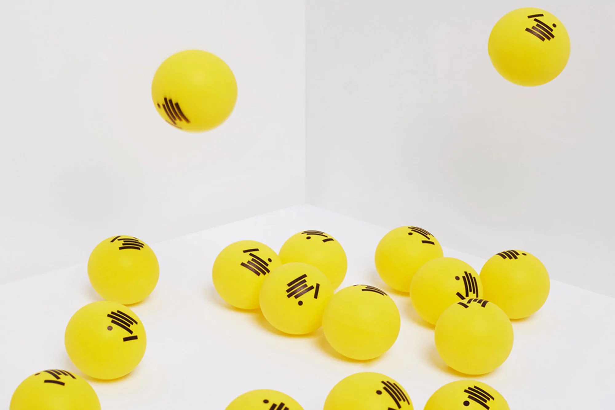 Many yellow-colored balls with black markings scattered on a white surface in a white corner, some appear to be floating.