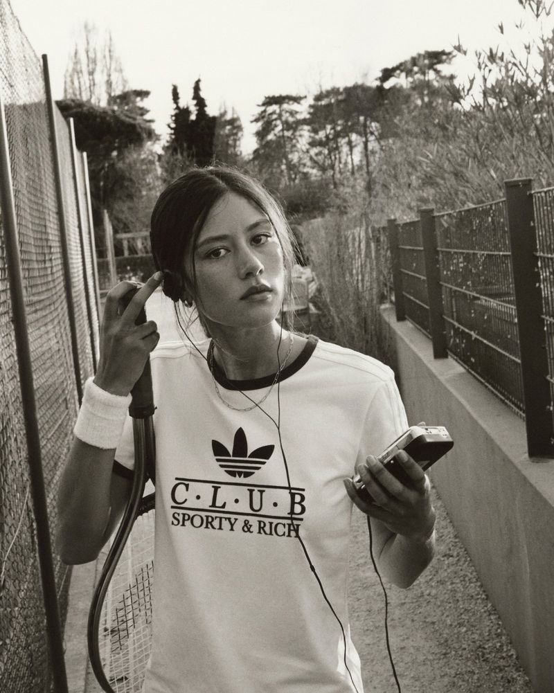 Young woman in sporty t-shirt with wristband outdoors, listening to music with vintage player against a backdrop of green trees.