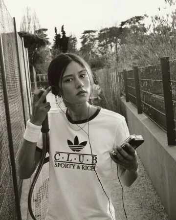 Young woman in sporty t-shirt with wristband outdoors, listening to music with vintage player against a backdrop of green trees.